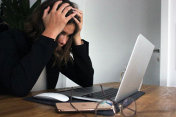 frustrated woman at her computer holding her head in her hands due to SBA loan required paperwork