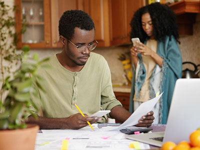 husband and wife in kitchen and husband is going through a mountain of bills using a calculator trying to figure out how they will pay them