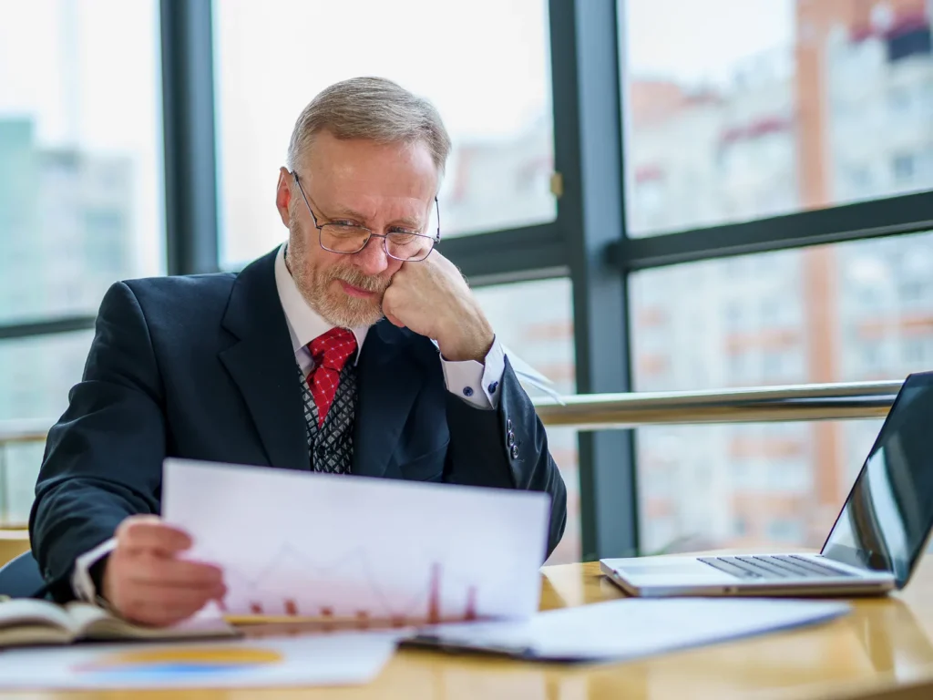 attorney frustrated with his finances looking at charts and tables with a laptop to his right. attorney frustrated with his finances looking at charts and tables with a laptop to his right.